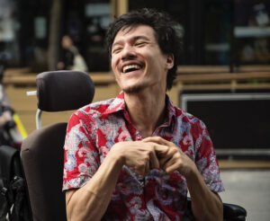 Young man with cerebral palsy laughing outdoors in city. He is using a wheelchair.